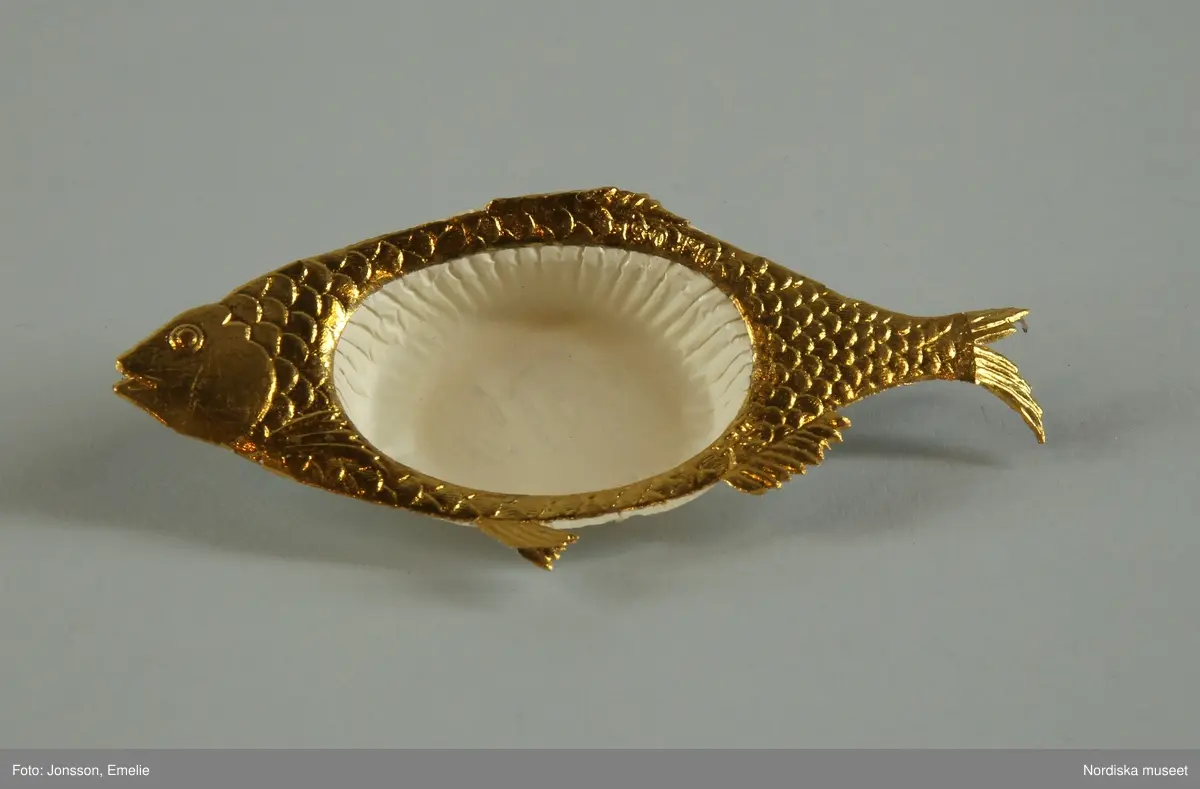 Huvudliggaren:
"Pappersformar, 5 st, papper veckade, pressat om ramning i form av en fisk; olika färger; före 1880. Gåva 20/11 1933 av fröken Dagmar Landelius, Stockholm."

Bilaga:
"En samling föremål från Landelius Kungl. hovkonditori, Storkyrkobrinken 9, Stockholm, skänkta av fröken Dagmar Landelius. Givarinnans morfar, J. C. Landelius, öppnade 1858 affären på Storkyrkobrinken. På 1860-talet öppnade samma firma den s.k. paviljongen på Drottningholm, vilken ombyggdes 1903. Affärsrörelsen på Storkyrkobrinken drevs till 1910, då huset skulle rivas, varför huvudaffären flyttades till Strandvägen 7A samt en filial till 16 Storkyrkobrinken.
I den gamla affären skyltades med två speldosor (nr 194.909 och 194.921), samt en hare, som spelade på trumma, och en docka (194.921), vilken kläddes i olika dräkter efter årstiderna och samma docka hade även en sorgdräkt från 1870-talet, vilken användes vid kungssorg.
Slottet gjorde alla sina beställningar hos Landelius. Den 24 januari var det oftast bjudning med minst 1 000 karameller beställda. Drottning Sophia beställde Jesusbarn med gloria till småprinsessornas julgran samt tomtar och dylikt. Senare flyttade kronprinsparet över sina beställningar till annan firma, men de övriga kungliga gjorde fortfarande sina inköp hos Landelius, liksom flera andra större restauranger.
I det s.k. 'änglaskåpet' i affären på Storkyrkobrinken förvarades små figurer av dragant förfärdigade av fröken Beda Pegel, Karlavägen. Hon gjorde stora figurer till krokaner, begravningsföremål såsom biblar, kors och lamm etc. och till flyttgröt, tomtar med grötfat, samt till barndop lindebarn burna av storkar.
Från Paris tog man hem diverse små prydnadssaker till karameller. Firman Lumarier hade små verkstäder för olika material; vax, metall och bensaker allt utfört för hand. Små soffor och biljarder av ben lades som överraskningar i påskäggen.
Alla karameller inlades i affären och pryddes på olika sätt: svanen lades på en spegel med gräskant osv. Även efterrätter beställdes och om man t.ex. önskade ett lapplandskap gjordes kåtan av bakverk med snöbollar av spunnet socker medan renen och lapparna voro skurna i trä och återtogs dagen därpå. Denna efterrätt var synnerligen omtyckt på 1890-talets början."