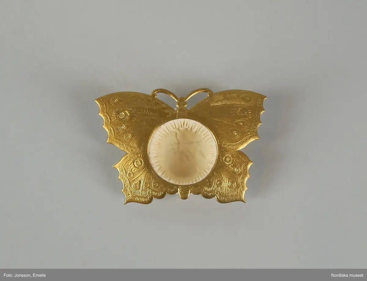 Huvudliggaren:
"Pappersformar, 9 st, papper veckade, omramning i form av en stor fjäril, mönstrat papper i olika färger; före år 1880. Gåva 20/11 1933 av fröken Dagmar Landelius, Stockholm."

Bilaga:
"En samling föremål från Landelius Kungl. hovkonditori, Storkyrkobrinken 9, Stockholm, skänkta av fröken Dagmar Landelius. Givarinnans morfar, J. C. Landelius, öppnade 1858 affären på Storkyrkobrinken. På 1860-talet öppnade samma firma den s.k. paviljongen på Drottningholm, vilken ombyggdes 1903. Affärsrörelsen på Storkyrkobrinken drevs till 1910, då huset skulle rivas, varför huvudaffären flyttades till Strandvägen 7A samt en filial till 16 Storkyrkobrinken.
I den gamla affären skyltades med två speldosor (nr 194.909 och 194.921), samt en hare, som spelade på trumma, och en docka (194.921), vilken kläddes i olika dräkter efter årstiderna och samma docka hade även en sorgdräkt från 1870-talet, vilken användes vid kungssorg.
Slottet gjorde alla sina beställningar hos Landelius. Den 24 januari var det oftast bjudning med minst 1 000 karameller beställda. Drottning Sophia beställde Jesusbarn med gloria till småprinsessornas julgran samt tomtar och dylikt. Senare flyttade kronprinsparet över sina beställningar till annan firma, men de övriga kungliga gjorde fortfarande sina inköp hos Landelius, liksom flera andra större restauranger.
I det s.k. 'änglaskåpet' i affären på Storkyrkobrinken förvarades små figurer av dragant förfärdigade av fröken Beda Pegel, Karlavägen. Hon gjorde stora figurer till krokaner, begravningsföremål såsom biblar, kors och lamm etc. och till flyttgröt, tomtar med grötfat, samt till barndop lindebarn burna av storkar.
Från Paris tog man hem diverse små prydnadssaker till karameller. Firman Lumarier hade små verkstäder för olika material; vax, metall och bensaker allt utfört för hand. Små soffor och biljarder av ben lades som överraskningar i påskäggen.
Alla karameller inlades i affären och pryddes på olika sätt: svanen lades på en spegel med gräskant osv. Även efterrätter beställdes och om man t.ex. önskade ett lapplandskap gjordes kåtan av bakverk med snöbollar av spunnet socker medan renen och lapparna voro skurna i trä och återtogs dagen därpå. Denna efterrätt var synnerligen omtyckt på 1890-talets början."