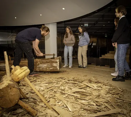 Presenter demonstrating traditional Viking boatbuilding with axe in front of engaged students.