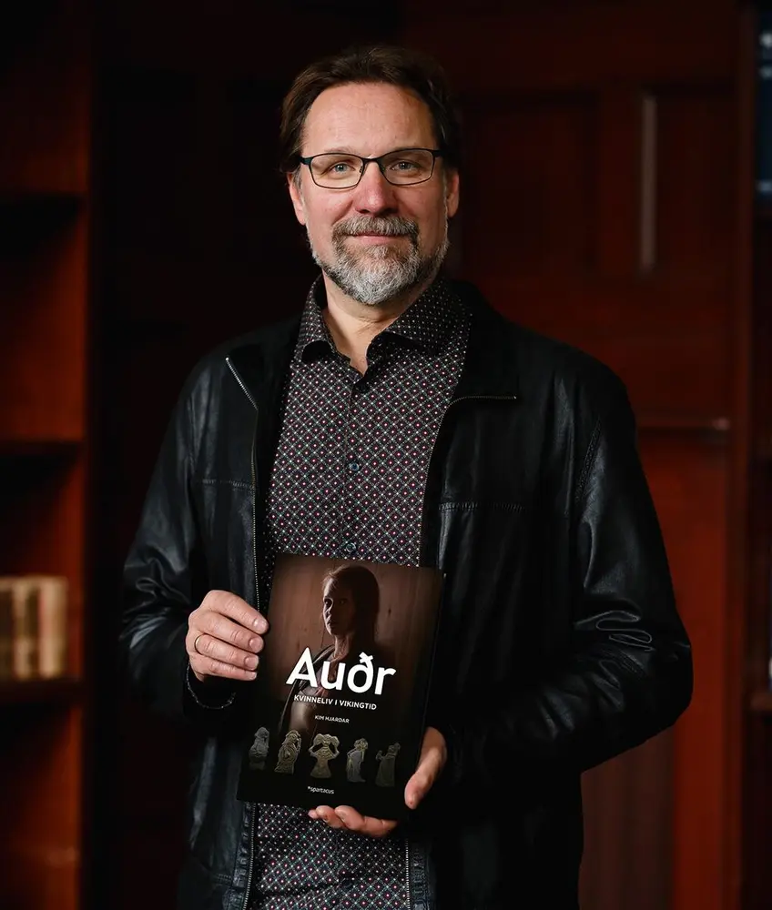 Bilde av historiker og forfatter Kim Hjardar. Han holder en bok i hånden og smiler mot kameraet.