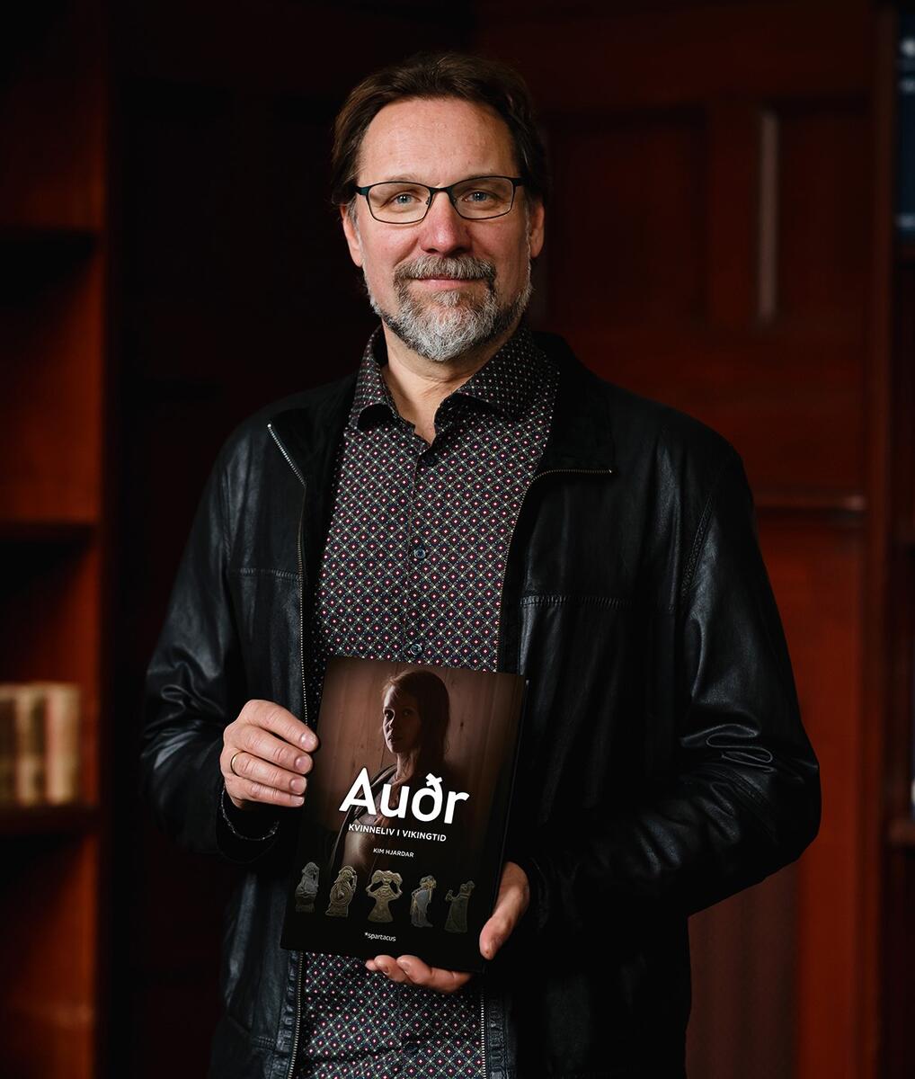 Bilde av historiker og forfatter Kim Hjardar. Han holder en bok i hånden og smiler mot kameraet.