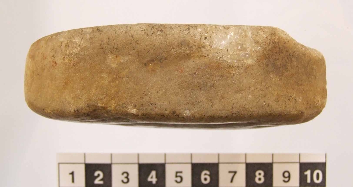 Eldslagningssten med spetsoval form. Grund ränna på smalsidorna. Kort något snedställt slagspår på en flatsidan och ett grunt något snedställt slagspår på den andra flatsidan. Något skadad i ena änden.