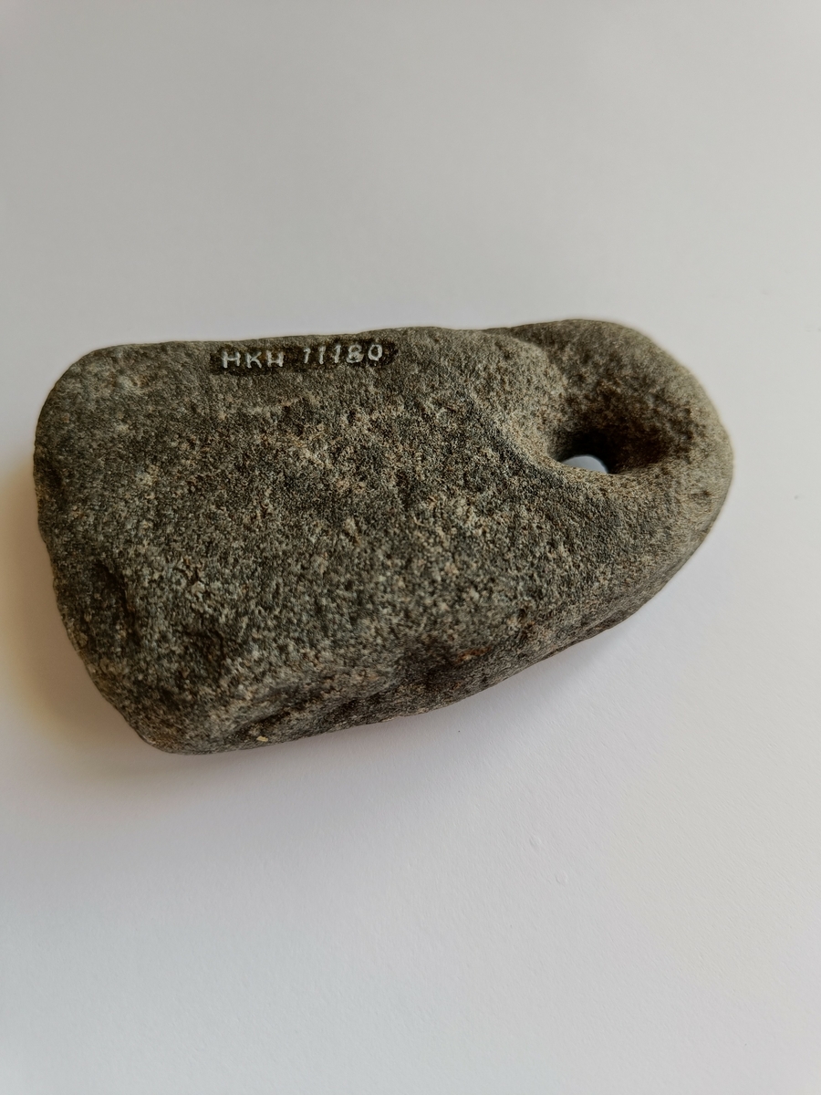 En avlang og ganske flat stein med et boret hull i den smaleste enden.