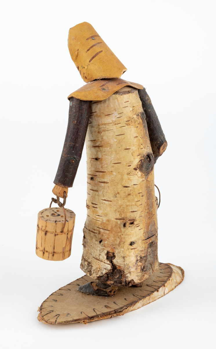 Trefigur spikket av tre, med påmontert never. Figuren er festet til en treplate.
Figuren er en etterligning etter moren til Eldbjørg Kordal, Ellen Pauline (f. Einarsrud) Kordal. Kona bærer ei vannbøtte i hver hand. Trefiguren var en gave fra Eldbjørg og hennes far jula 1967.