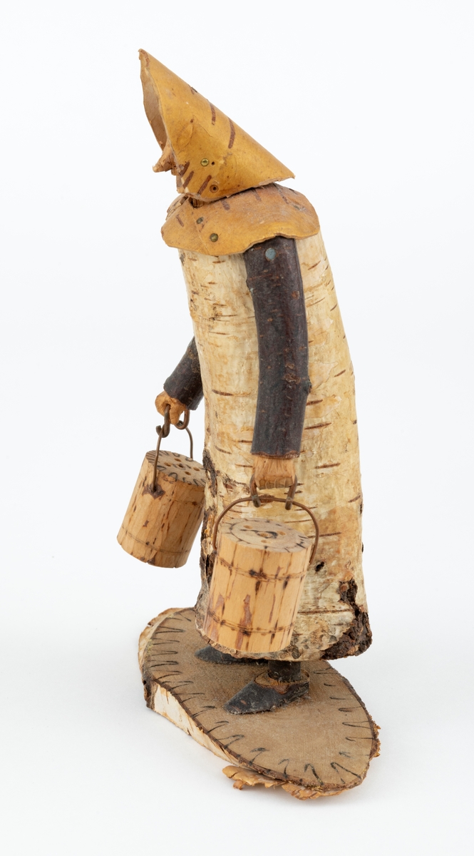 Trefigur spikket av tre, med påmontert never. Figuren er festet til en treplate.
Figuren er en etterligning etter moren til Eldbjørg Kordal, Ellen Pauline (f. Einarsrud) Kordal. Kona bærer ei vannbøtte i hver hand. Trefiguren var en gave fra Eldbjørg og hennes far jula 1967.