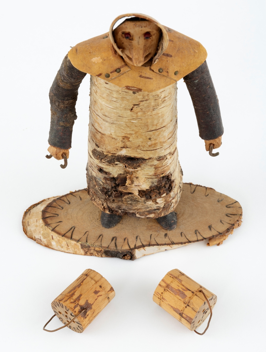 Trefigur spikket av tre, med påmontert never. Figuren er festet til en treplate.
Figuren er en etterligning etter moren til Eldbjørg Kordal, Ellen Pauline (f. Einarsrud) Kordal. Kona bærer ei vannbøtte i hver hand. Trefiguren var en gave fra Eldbjørg og hennes far jula 1967.