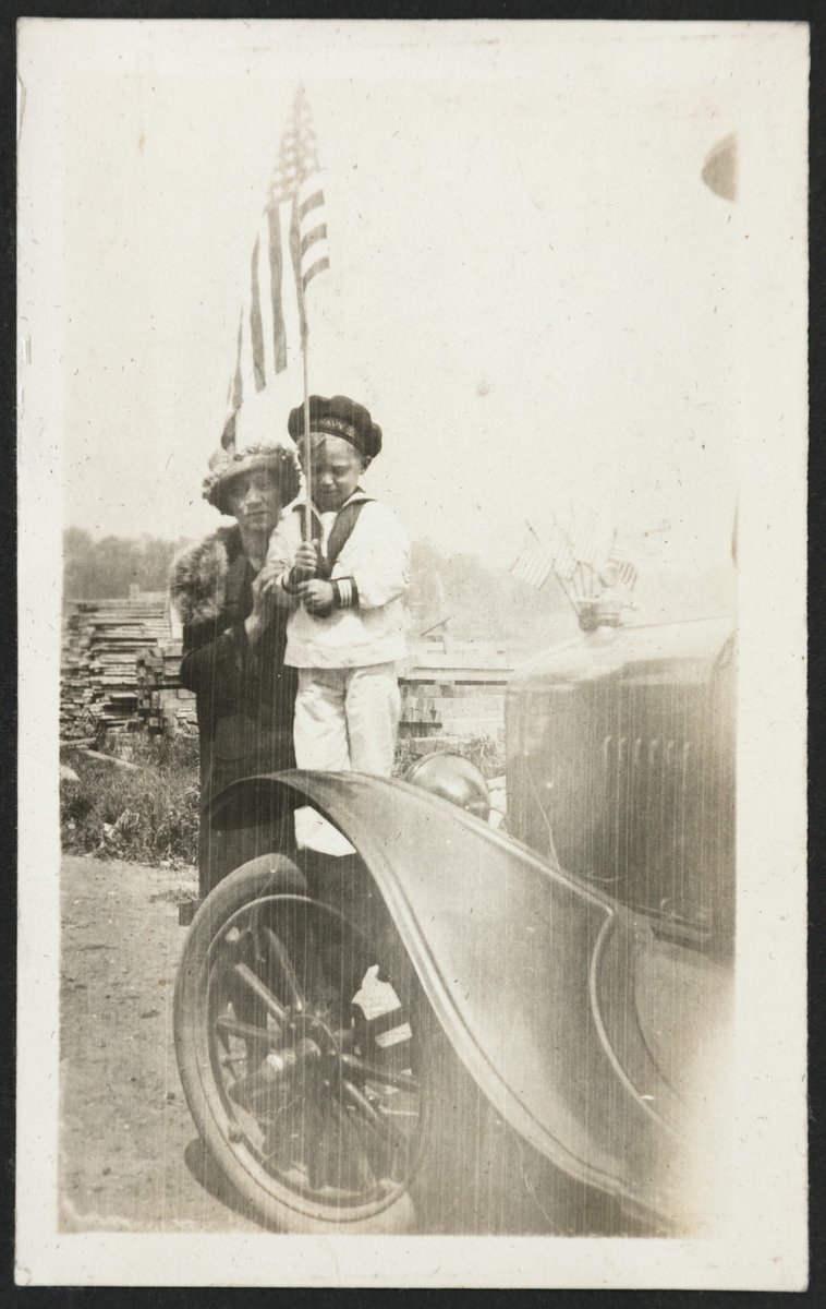 Mrs. Ragnhild Bang og sønnen Billy ved panseret på en bil i Ouster ave. Billy har matrosdress og et amerikansk flagg. Også bilen er pyntet med små flagg.