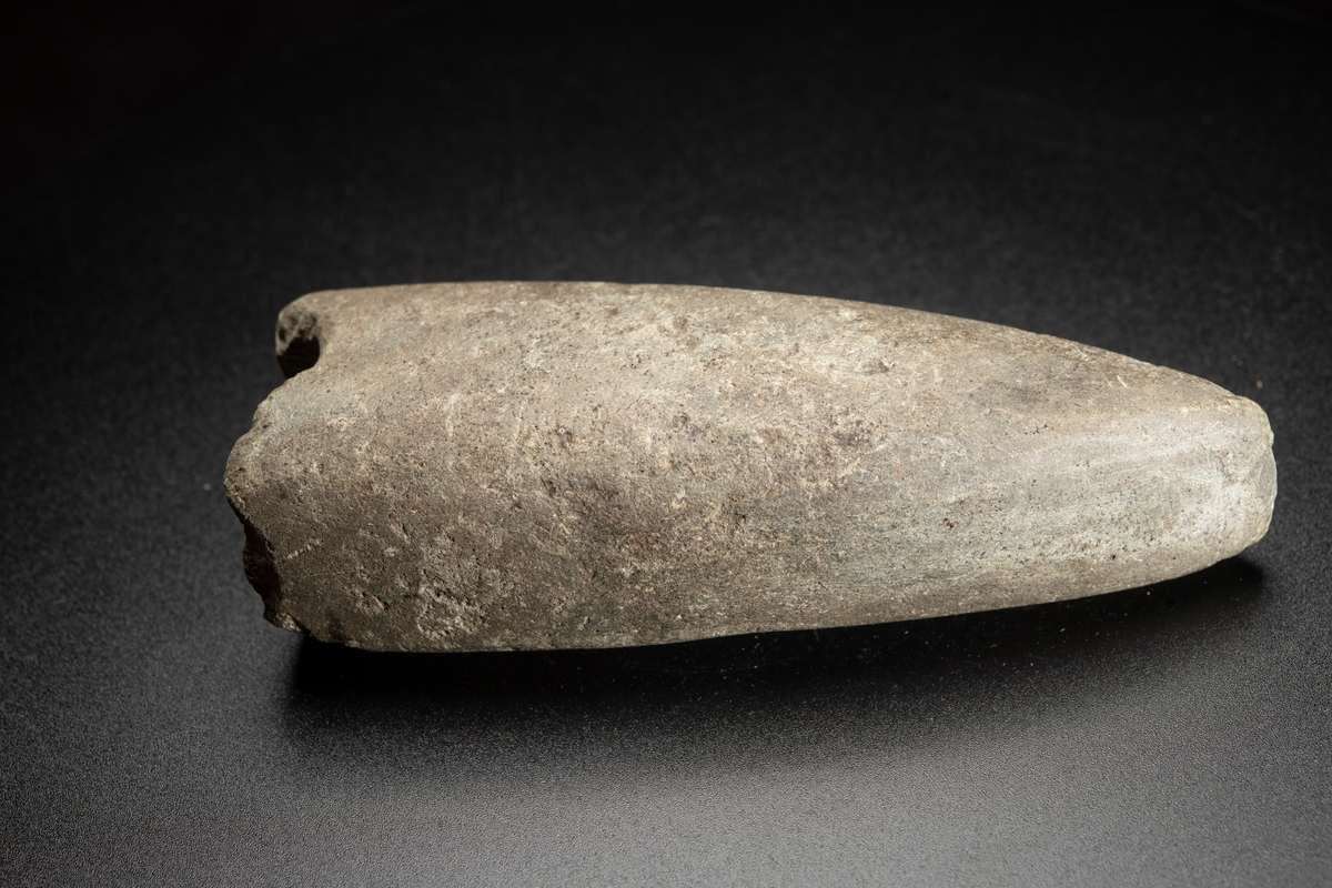 Eggparti. Yxan avslagen över skafthålet. Långsträckt, långsmal form. Skafthålet placerat långt bakåt. Helt slipad.