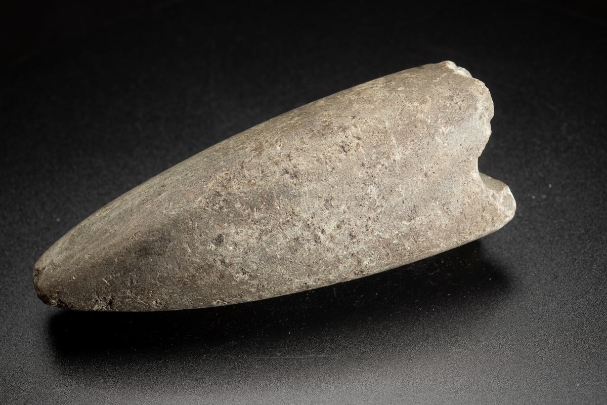 Eggparti. Yxan avslagen över skafthålet. Långsträckt, långsmal form. Skafthålet placerat långt bakåt. Helt slipad.