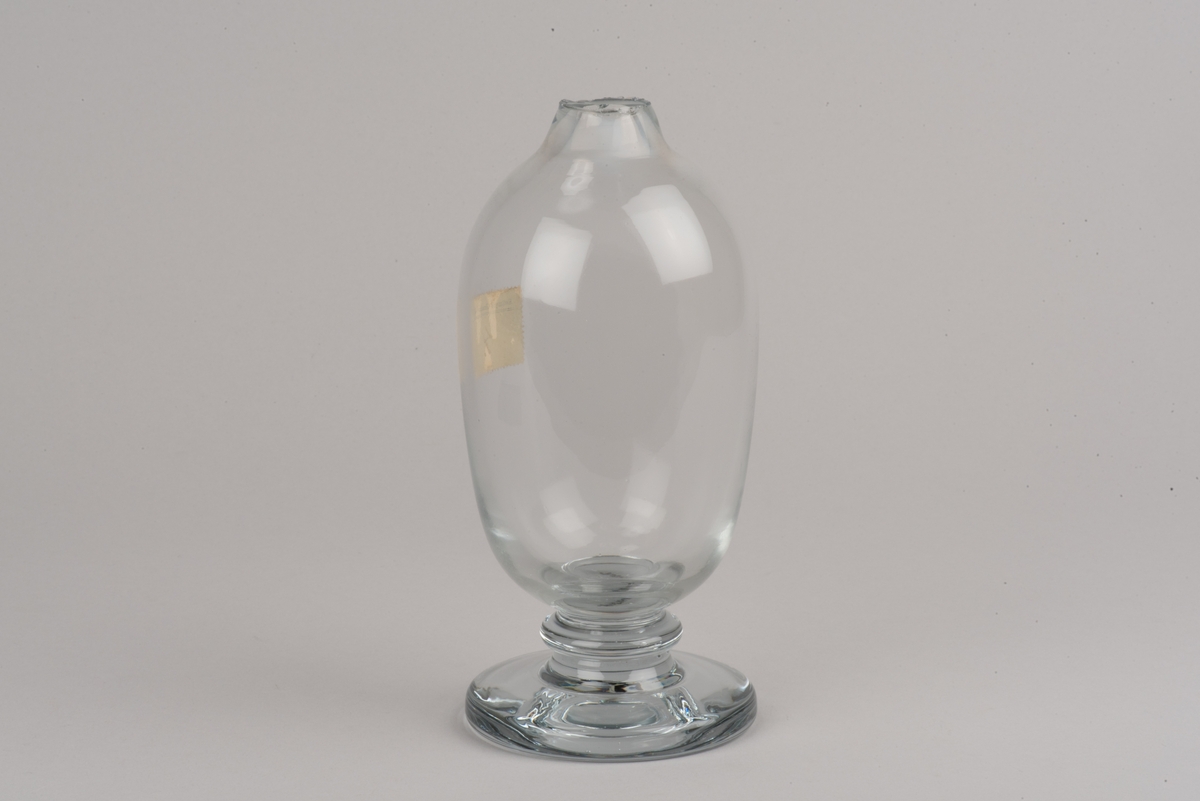 Ämne till kanna av drivet glas. 
Oval kanna som smalnar av mot fot och mynning. Rund, påklippt fot.