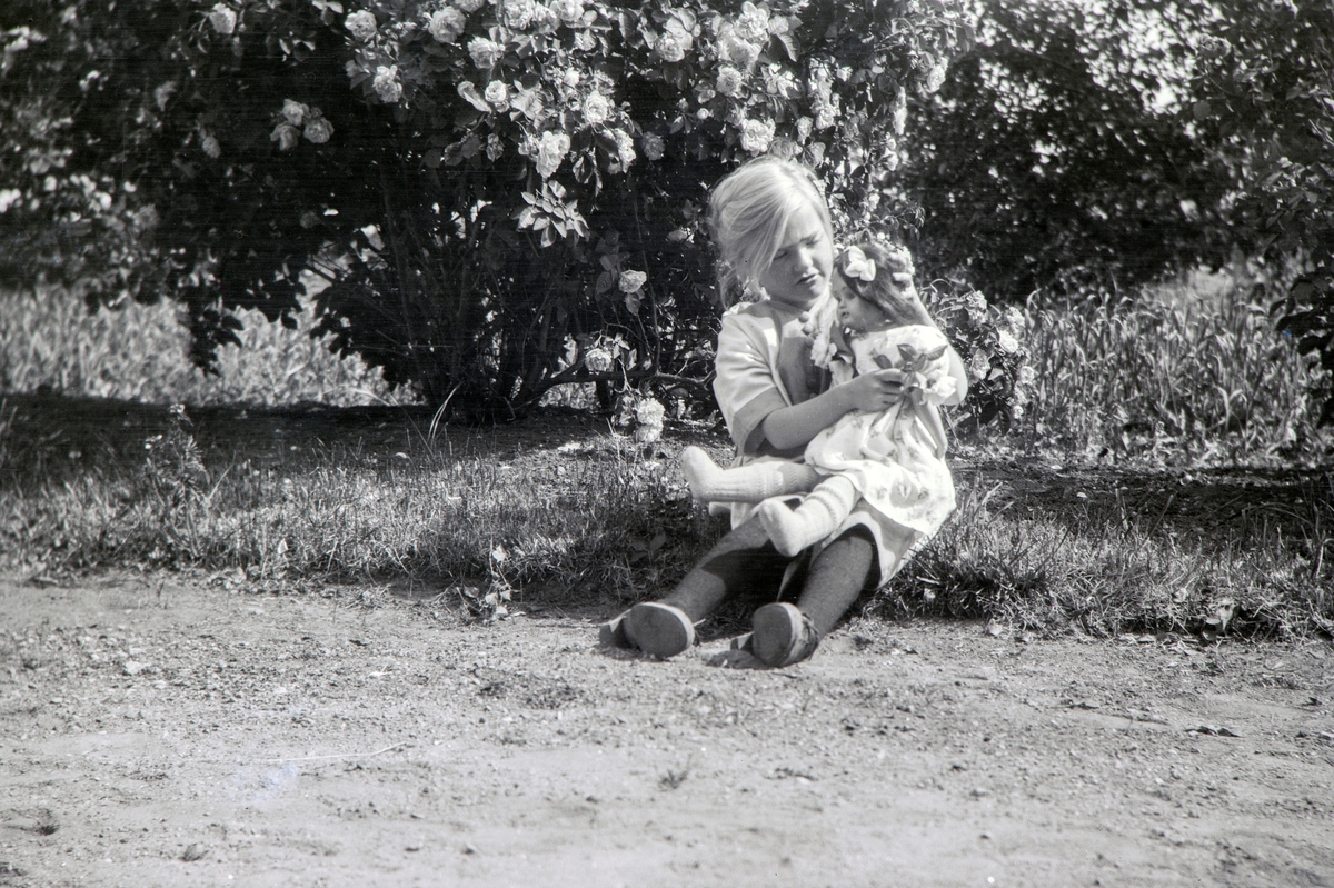 På Ottestad Nordre. Andrea Margrethe Glærum, født Gjestvang (1914-1993) leker med dokke ute i hagen, i 1917