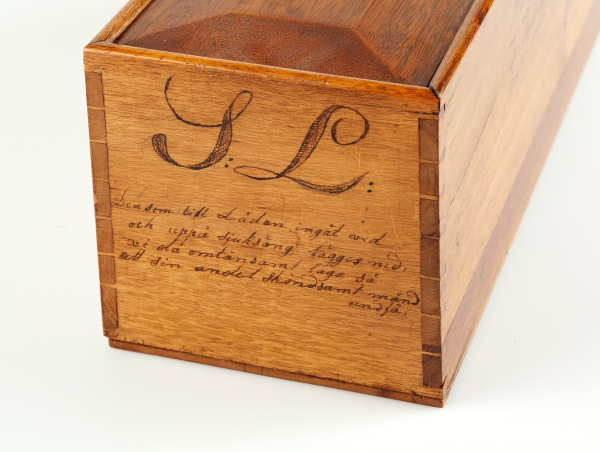Låda med skjutlock. Mörkare trä. Lackad. På locket inbränt: Sjuk=låda. På kortändarna S:L: och poem.