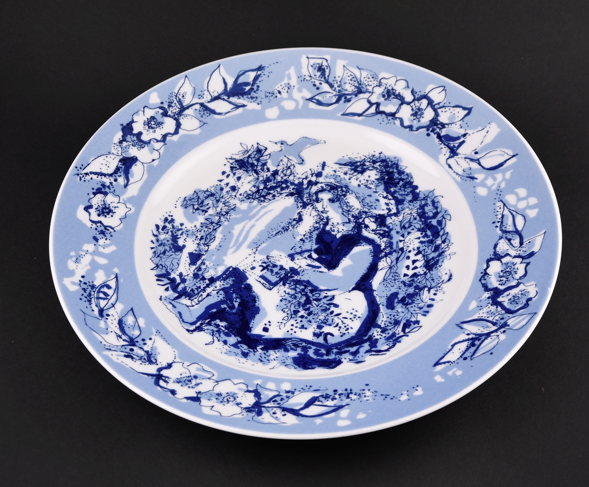 Tallerken av porselen med blått og hvitt trykk. På kanten er det rander med blomster. På midten er det motiv fra Bjørnstjerne Bjørnsons fortelling Arne. Tallerkenen har hull bak for oppheng.
