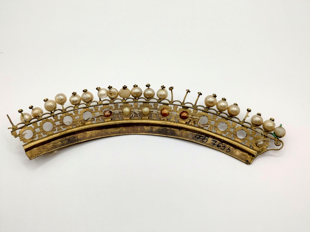 Pyntekam bestående av to deler. Den ene delen (a) er en 3cm høy gjennombrutt metallplate som er pyntet med uekte perler. PÅ baksiden er det påloddet åtte horisontale metalltråder. Den andre delen (b) er likt dekorert, men er lengre og buet. Den har ikke metalltråder på baksiden.