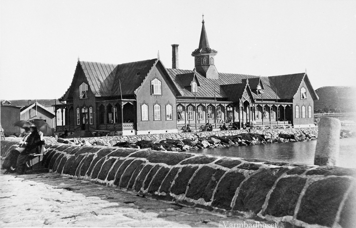 Varmbadhuset i Varberg, uppfört 1866. I förgrunden hamnpirens vågbrytare där ett par kvinnor sitter under parasoller.