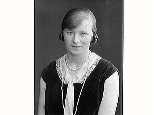 Porträtt av ung kvinna. Agnes Andersson från Lidarna Hunnestad, klädd i ärmlös klänning som har både spetskrage och slips. Långt pärlhalsband.
