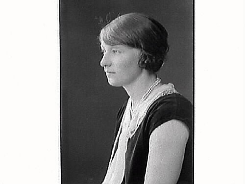 Porträtt av ung kvinna. Agnes Andersson från Lidarna Hunnestad, klädd i ärmlös klänning som har både spetskrage och slips. Långt pärlhalsband.