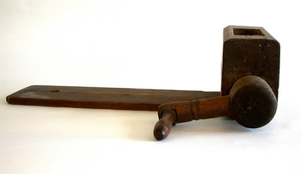 Kvarn av trä. a) Längd 25 cm b) 32 cm c) 21,5 cm. För malning av kokt potatis. Matas uppifrån genom fyrkantig öppning där potatisen pressas ned med handtag (c).
