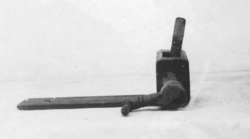 Kvarn av trä. a) Längd 25 cm b) 32 cm c) 21,5 cm. För malning av kokt potatis. Matas uppifrån genom fyrkantig öppning där potatisen pressas ned med handtag (c).