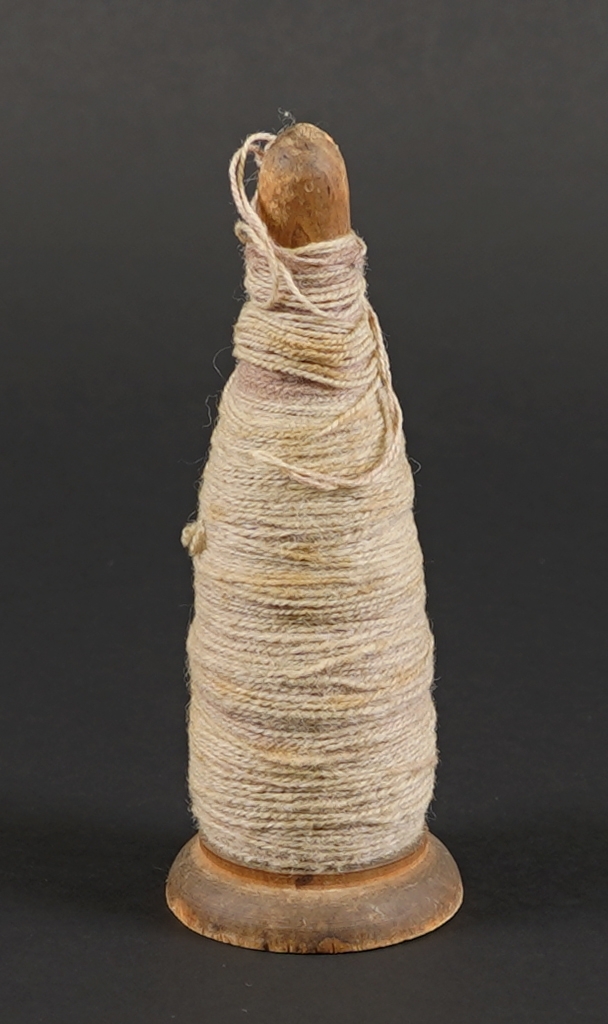 Ein spole med ullgarn. Spolen er dreia i tre.