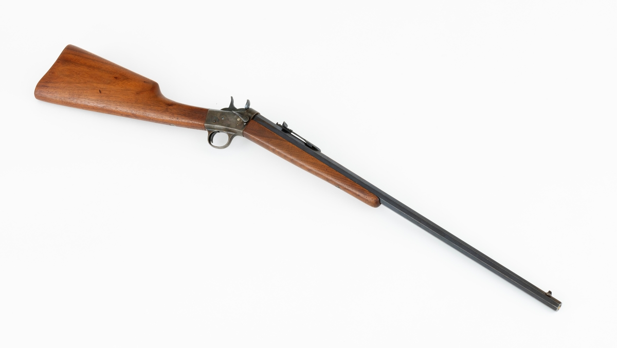 Tillegg innskrift: Remington TRADE MARK MODEL 4 25-10 R. F. Geværet har brunt, oljebehandlet treverk. Framstillingsnummeret er J 304870. Laget ca. 1870. Av størrelse kan geværet se ut som ei salongrifle, men kaliberet, 25-10, er litt større enn på Krag. R. F. står for Rand Fire (randtenning. ) 10-tallet står for 10 gram svartkrutt. Dvs. ca. 4 gram. Dette er en meget kraftig ladning, nesten like mye som på den store Remington. Det må være en av de raskeste svartkruttpatroner som er laget.