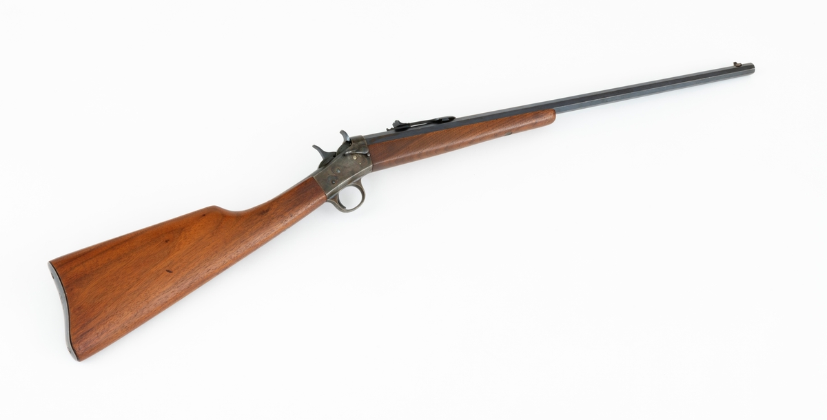 Tillegg innskrift: Remington TRADE MARK MODEL 4 25-10 R. F. Geværet har brunt, oljebehandlet treverk. Framstillingsnummeret er J 304870. Laget ca. 1870. Av størrelse kan geværet se ut som ei salongrifle, men kaliberet, 25-10, er litt større enn på Krag. R. F. står for Rand Fire (randtenning. ) 10-tallet står for 10 gram svartkrutt. Dvs. ca. 4 gram. Dette er en meget kraftig ladning, nesten like mye som på den store Remington. Det må være en av de raskeste svartkruttpatroner som er laget.