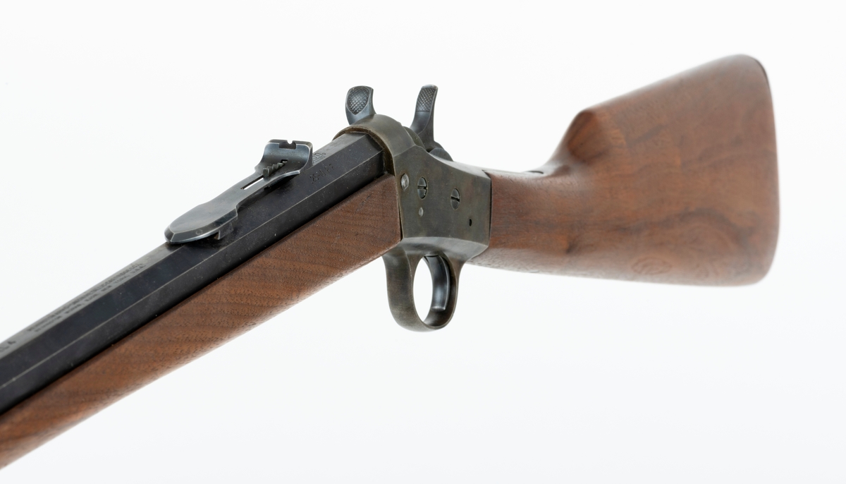 Tillegg innskrift: Remington TRADE MARK MODEL 4 25-10 R. F. Geværet har brunt, oljebehandlet treverk. Framstillingsnummeret er J 304870. Laget ca. 1870. Av størrelse kan geværet se ut som ei salongrifle, men kaliberet, 25-10, er litt større enn på Krag. R. F. står for Rand Fire (randtenning. ) 10-tallet står for 10 gram svartkrutt. Dvs. ca. 4 gram. Dette er en meget kraftig ladning, nesten like mye som på den store Remington. Det må være en av de raskeste svartkruttpatroner som er laget.