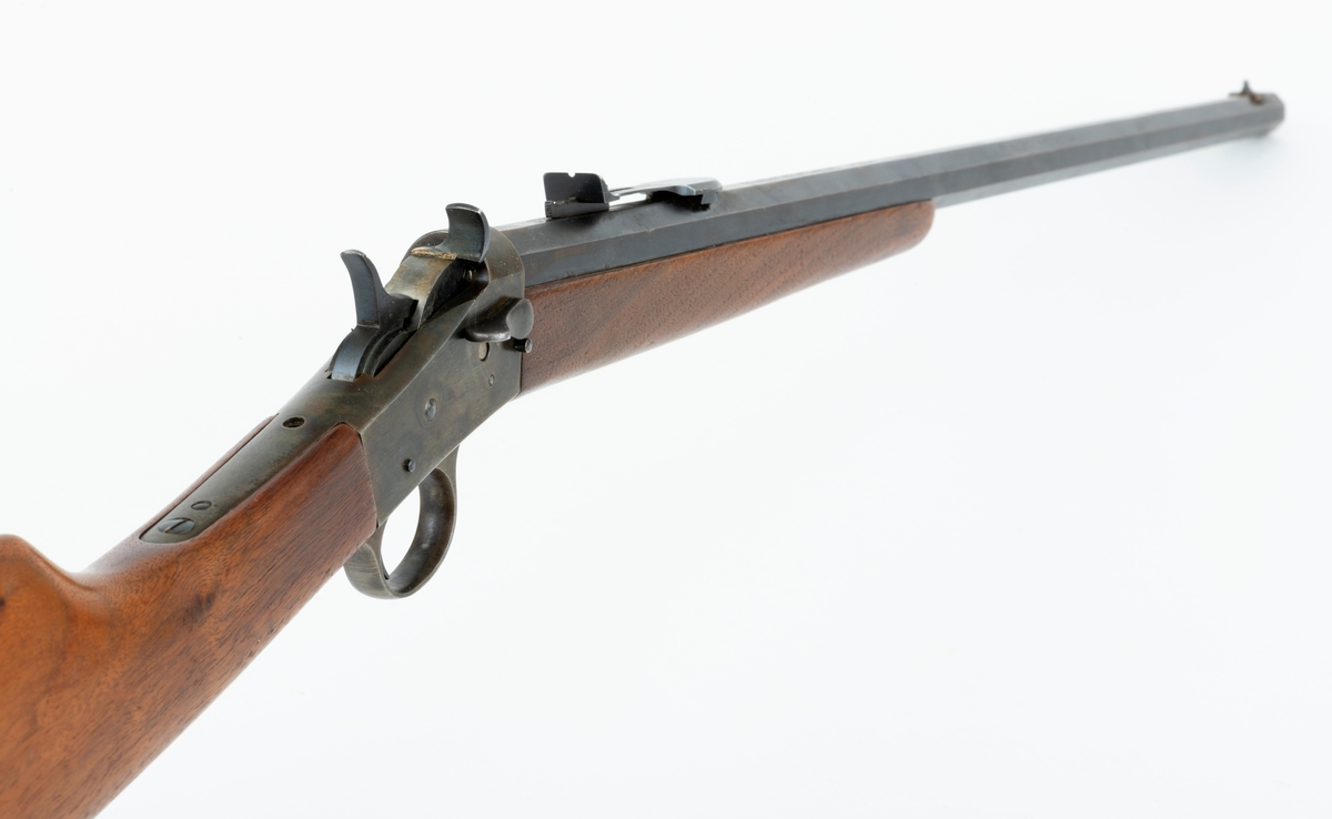 Tillegg innskrift: Remington TRADE MARK MODEL 4 25-10 R. F. Geværet har brunt, oljebehandlet treverk. Framstillingsnummeret er J 304870. Laget ca. 1870. Av størrelse kan geværet se ut som ei salongrifle, men kaliberet, 25-10, er litt større enn på Krag. R. F. står for Rand Fire (randtenning. ) 10-tallet står for 10 gram svartkrutt. Dvs. ca. 4 gram. Dette er en meget kraftig ladning, nesten like mye som på den store Remington. Det må være en av de raskeste svartkruttpatroner som er laget.