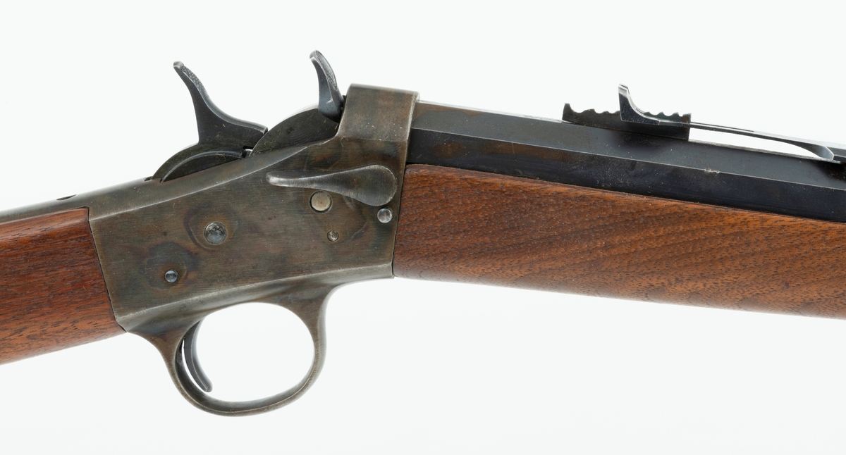 Tillegg innskrift: Remington TRADE MARK MODEL 4 25-10 R. F. Geværet har brunt, oljebehandlet treverk. Framstillingsnummeret er J 304870. Laget ca. 1870. Av størrelse kan geværet se ut som ei salongrifle, men kaliberet, 25-10, er litt større enn på Krag. R. F. står for Rand Fire (randtenning. ) 10-tallet står for 10 gram svartkrutt. Dvs. ca. 4 gram. Dette er en meget kraftig ladning, nesten like mye som på den store Remington. Det må være en av de raskeste svartkruttpatroner som er laget.