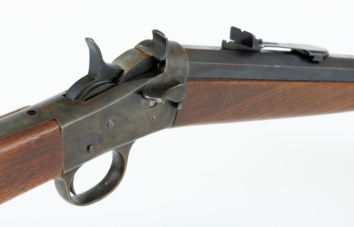 Tillegg innskrift: Remington TRADE MARK MODEL 4 25-10 R. F. Geværet har brunt, oljebehandlet treverk. Framstillingsnummeret er J 304870. Laget ca. 1870. Av størrelse kan geværet se ut som ei salongrifle, men kaliberet, 25-10, er litt større enn på Krag. R. F. står for Rand Fire (randtenning. ) 10-tallet står for 10 gram svartkrutt. Dvs. ca. 4 gram. Dette er en meget kraftig ladning, nesten like mye som på den store Remington. Det må være en av de raskeste svartkruttpatroner som er laget.