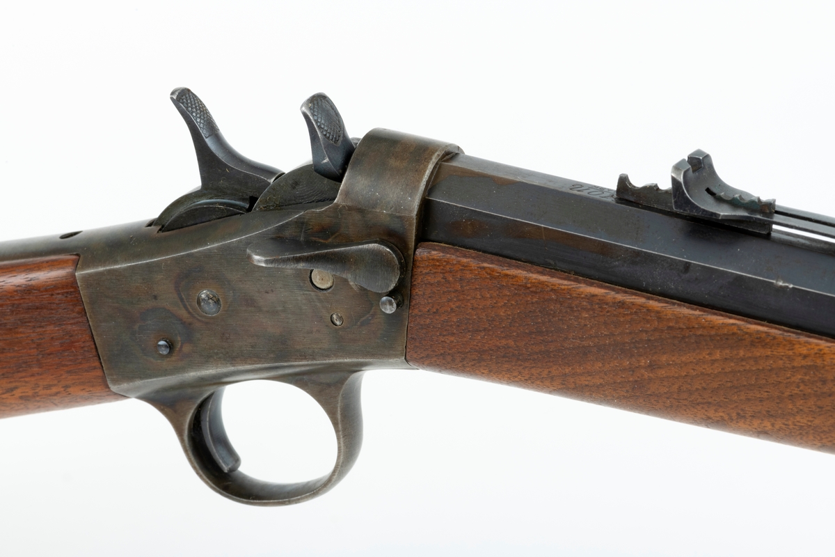 Tillegg innskrift: Remington TRADE MARK MODEL 4 25-10 R. F. Geværet har brunt, oljebehandlet treverk. Framstillingsnummeret er J 304870. Laget ca. 1870. Av størrelse kan geværet se ut som ei salongrifle, men kaliberet, 25-10, er litt større enn på Krag. R. F. står for Rand Fire (randtenning. ) 10-tallet står for 10 gram svartkrutt. Dvs. ca. 4 gram. Dette er en meget kraftig ladning, nesten like mye som på den store Remington. Det må være en av de raskeste svartkruttpatroner som er laget.