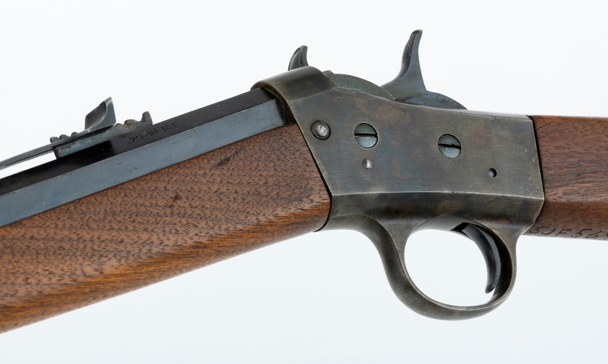 Tillegg innskrift: Remington TRADE MARK MODEL 4 25-10 R. F. Geværet har brunt, oljebehandlet treverk. Framstillingsnummeret er J 304870. Laget ca. 1870. Av størrelse kan geværet se ut som ei salongrifle, men kaliberet, 25-10, er litt større enn på Krag. R. F. står for Rand Fire (randtenning. ) 10-tallet står for 10 gram svartkrutt. Dvs. ca. 4 gram. Dette er en meget kraftig ladning, nesten like mye som på den store Remington. Det må være en av de raskeste svartkruttpatroner som er laget.