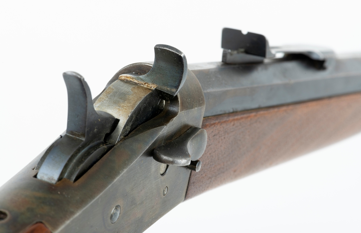 Tillegg innskrift: Remington TRADE MARK MODEL 4 25-10 R. F. Geværet har brunt, oljebehandlet treverk. Framstillingsnummeret er J 304870. Laget ca. 1870. Av størrelse kan geværet se ut som ei salongrifle, men kaliberet, 25-10, er litt større enn på Krag. R. F. står for Rand Fire (randtenning. ) 10-tallet står for 10 gram svartkrutt. Dvs. ca. 4 gram. Dette er en meget kraftig ladning, nesten like mye som på den store Remington. Det må være en av de raskeste svartkruttpatroner som er laget.