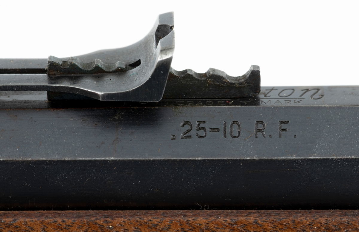 Tillegg innskrift: Remington TRADE MARK MODEL 4 25-10 R. F. Geværet har brunt, oljebehandlet treverk. Framstillingsnummeret er J 304870. Laget ca. 1870. Av størrelse kan geværet se ut som ei salongrifle, men kaliberet, 25-10, er litt større enn på Krag. R. F. står for Rand Fire (randtenning. ) 10-tallet står for 10 gram svartkrutt. Dvs. ca. 4 gram. Dette er en meget kraftig ladning, nesten like mye som på den store Remington. Det må være en av de raskeste svartkruttpatroner som er laget.