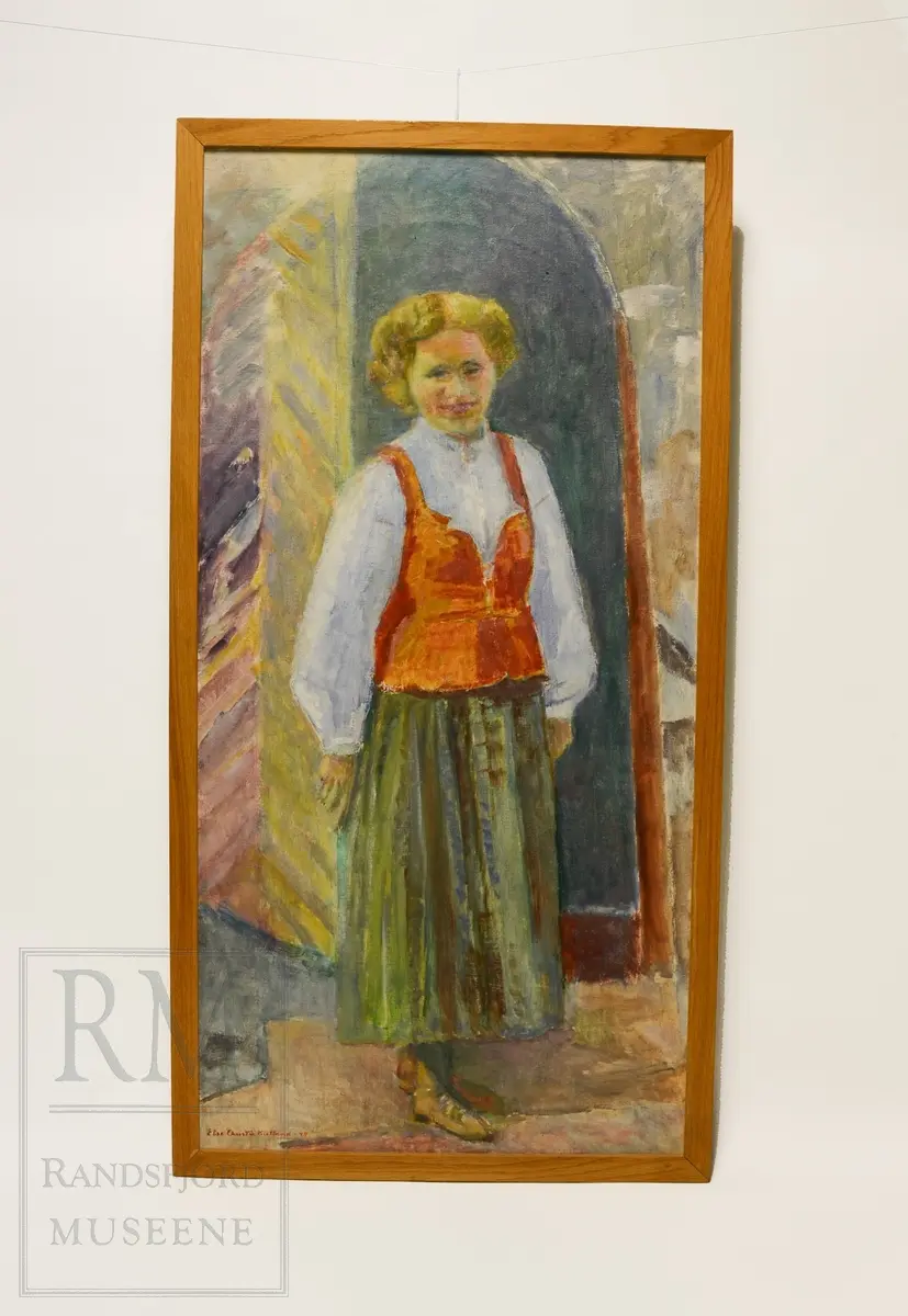 Helfigur. Kari Lander på trappen foran Tingelstad gml. kirke. Smiler. Grønn stakk med rødt liv og hvit skjorte med vide ermer. Rund sølje i halslinning.