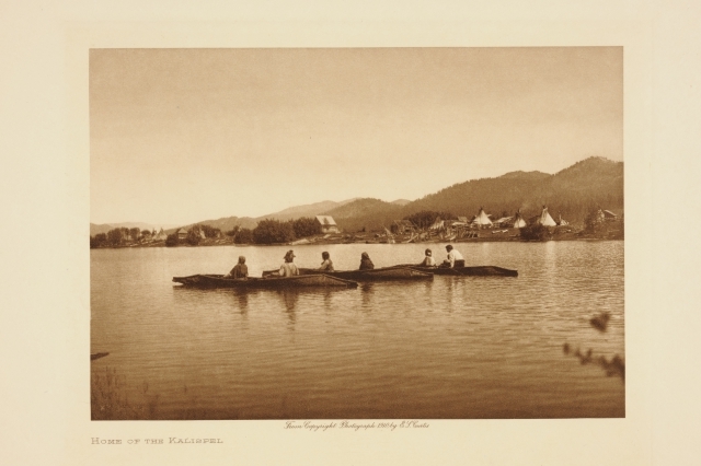 Tre kanoer på vannet. I bakgrunnen er det en teltplass og bebyggelse. Kalispel-stammen holdt til i området rundt Lake Pend Oreille, Idaho.