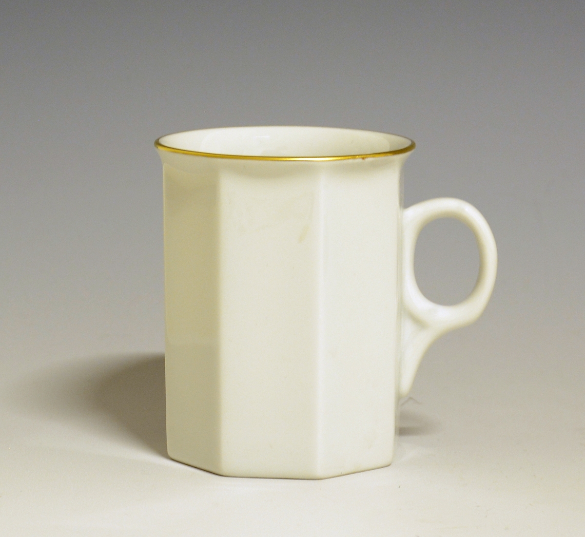 Mangekantet kopp i porselen med kantstrek i gull og logo i form av en rød gryte med lokk og påskriften "Til Bords". Hvit glasur.
Modell: Octavia, tegnet av Grete Rønning i 1977.