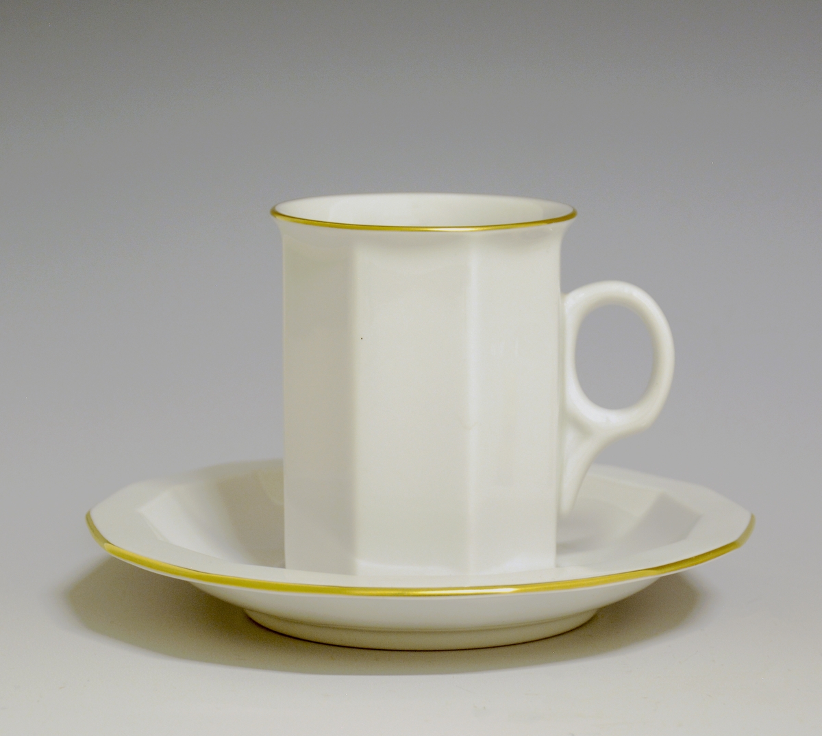 Mangekantet kopp i porselen med kantstrek i gull og logo i form av en rød gryte med lokk og påskriften "Til Bords". Hvit glasur.
Modell: Octavia, tegnet av Grete Rønning i 1977.
