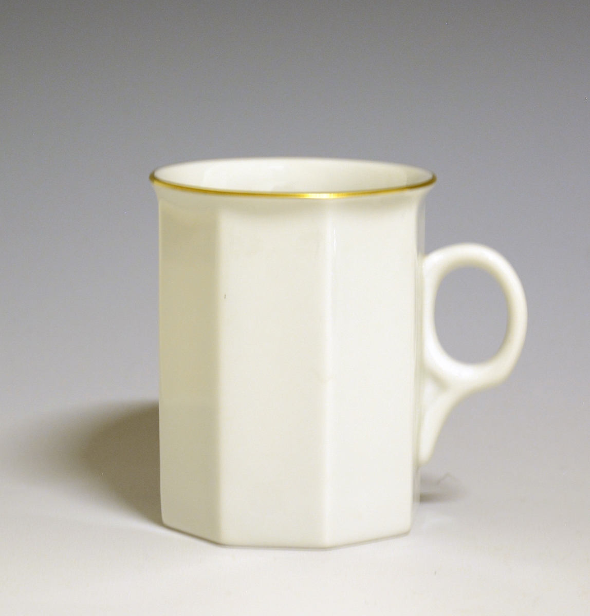 Mangekantet kopp i porselen med kantstrek i gull og logo i form av en rød gryte med lokk og påskriften "Til Bords". Hvit glasur.
Modell: Octavia, tegnet av Grete Rønning i 1977.
