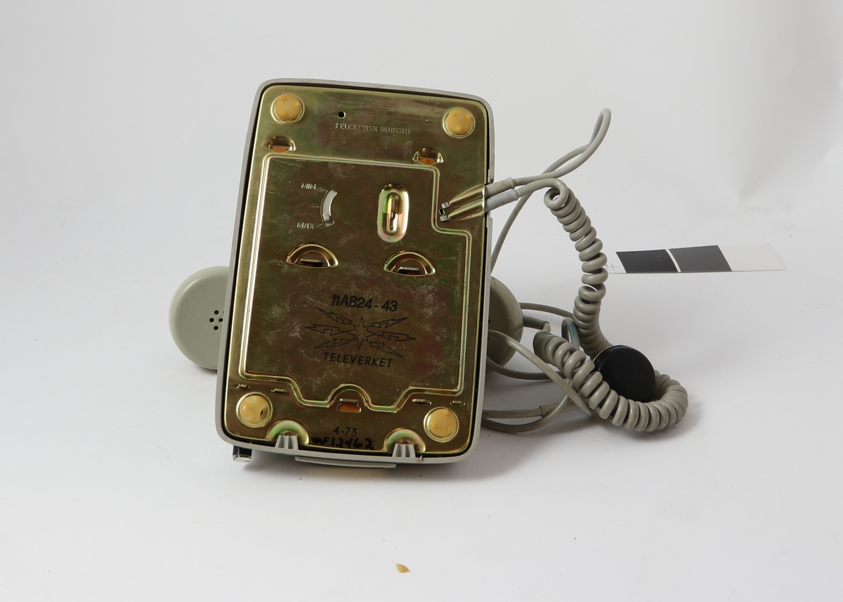 Grått telefonapparat av bakelitt med tilnærmet kvadratisk bunn og buet deksel med sirkulær tallskive.

