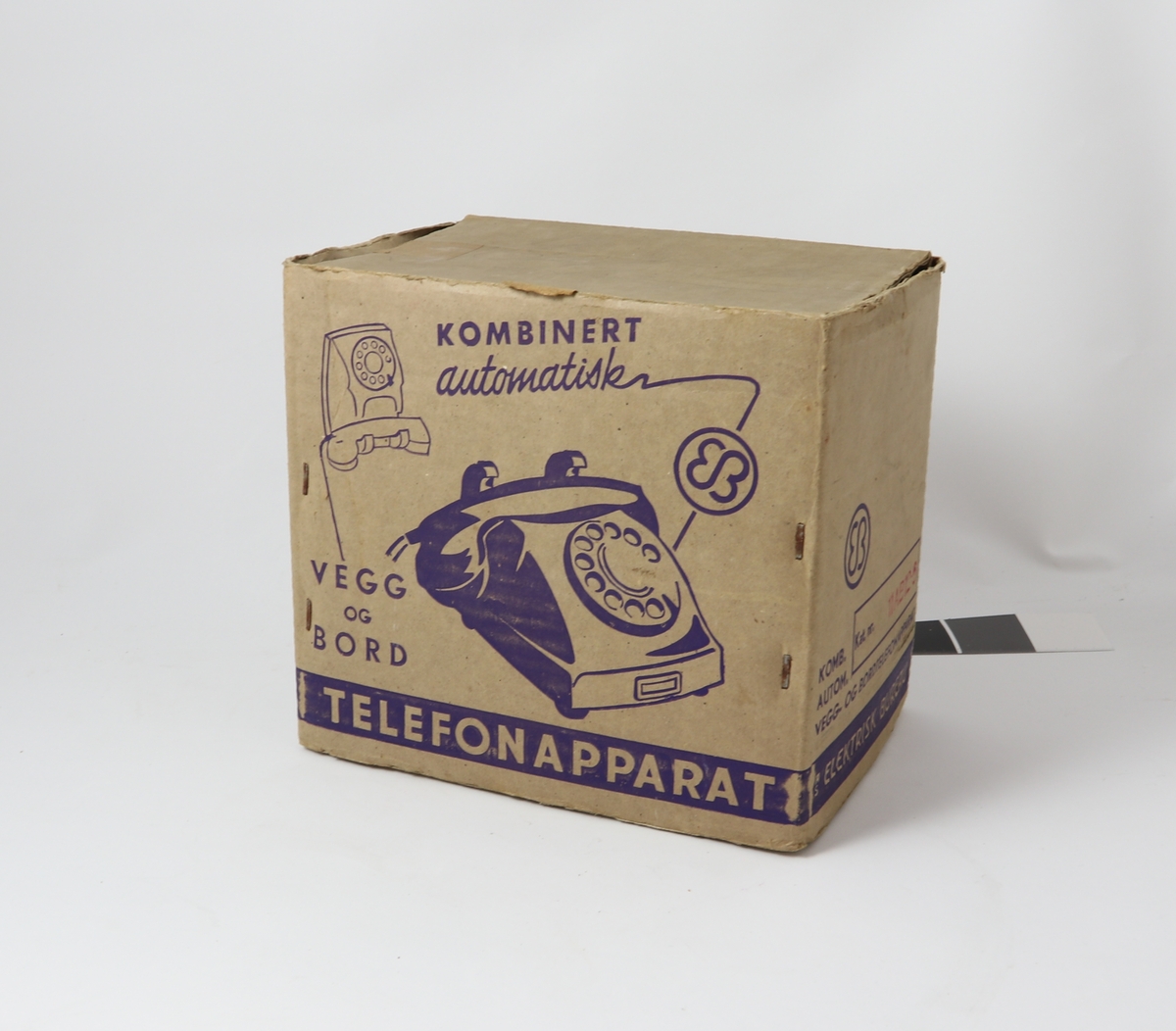 Grått telefonapparat av bakelitt med tilnærmet kvadratisk bunn og buet deksel med sirkulær tallskive.
