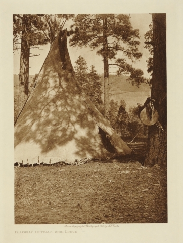 Et tipi av bøffelskinn i skogen. Til høyre henger et skjold.