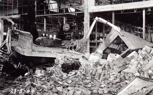 Sort-hvitt bilde av en nedrast bygning. Vi ser mengder med betong og armeringsjern.