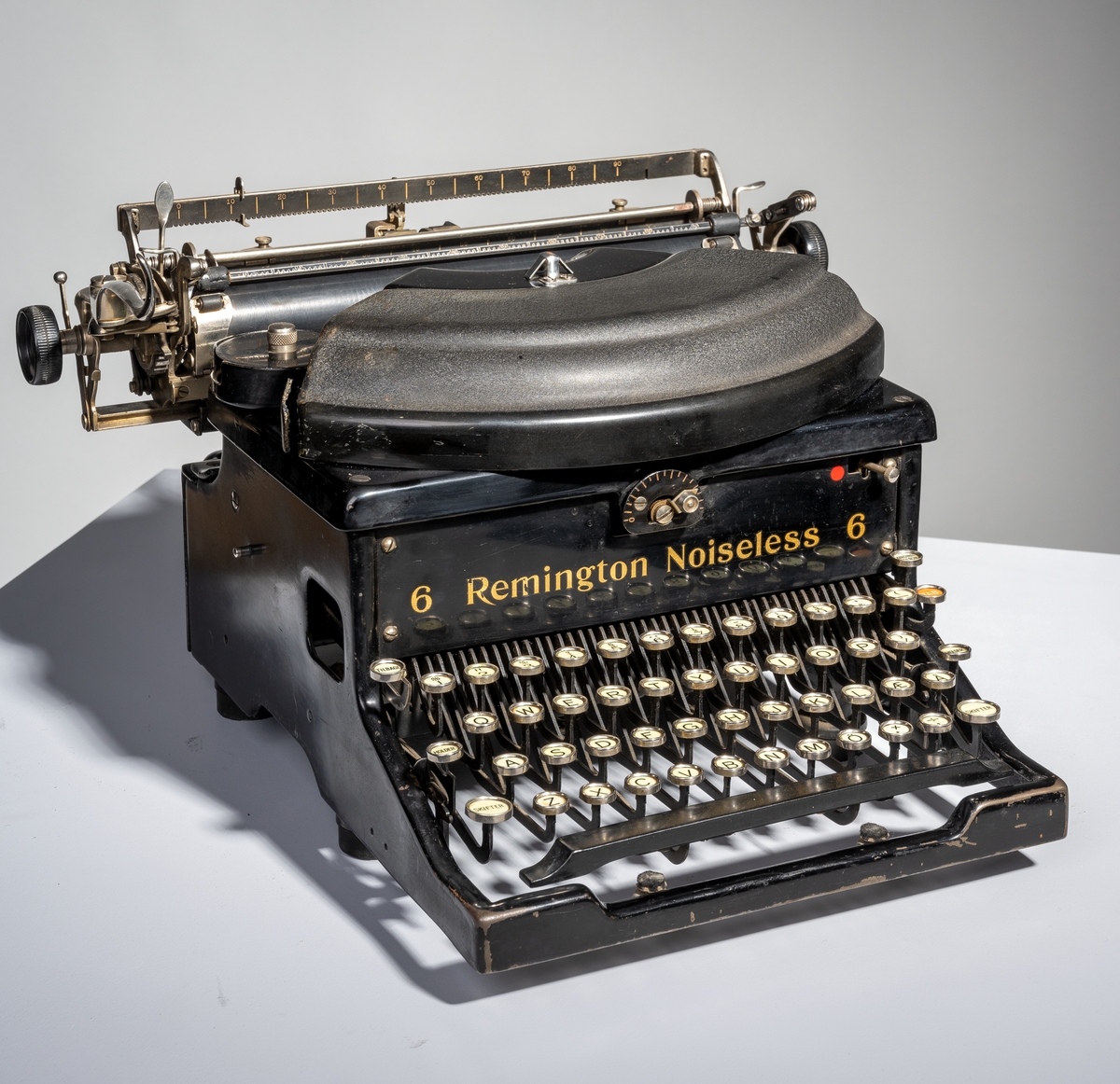 En skrivemaskin av typen "Remington Noiseless 6". Den er av svartlakkert metall med påført tekst i gullfarge. Den står på fire runde bein av svart gummi. Typearmene er festet i vifteform og over dem er det et deksle av svart bakelitt. På hver side av vifteformen er det runde holdere med deksel for å sette i fargebånd. I bakkant på maskinen er det stativ for å sett i papir. Papiret justeres med svarte plasthjul montert på hver ende av stativet. På venstre side er det et håndtak for å kunne skyve papiret opp to hakk. På stativet er det også tre linjaler/målestokker, to i bakkant og en i front. 
I front på skrivemaskinen er det tastatur. Det er tre rader med bokstaver med "dobbel shift" for henholdsvis store og små bokstaver. Nederst til høyre (nederste bokstavrekke) er det to taster med henholdsvis "+." og "-,". Øverst på tastaturet er det en rad med tall fra 1-0 samt ulike tegn som 
$ - % - § og så videre. Ytterst til venstre er det tre taster for henholdsvis "Tilbage", "Holder" og "Skifter". Ytterst til høyre er det fire taster for henholdsvis "Marginal udløsn.", "TAB", "Holder" og "SKifter. Nederst er det en avlang mellomromstast. Alle tastene er hvite med svart skrift unntatt "TAB" som er rød med hvit skrift og mellomromstasten som er svart. Til skrivemaskinen hørere det til et firkantet underlag av grønn filt og et trekk sydd av brunt kunststoff/skai.