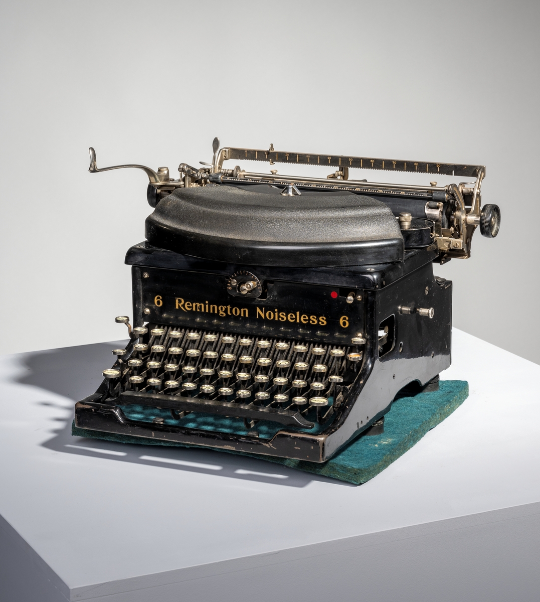 En skrivemaskin av typen "Remington Noiseless 6". Den er av svartlakkert metall med påført tekst i gullfarge. Den står på fire runde bein av svart gummi. Typearmene er festet i vifteform og over dem er det et deksle av svart bakelitt. På hver side av vifteformen er det runde holdere med deksel for å sette i fargebånd. I bakkant på maskinen er det stativ for å sett i papir. Papiret justeres med svarte plasthjul montert på hver ende av stativet. På venstre side er det et håndtak for å kunne skyve papiret opp to hakk. På stativet er det også tre linjaler/målestokker, to i bakkant og en i front. 
I front på skrivemaskinen er det tastatur. Det er tre rader med bokstaver med "dobbel shift" for henholdsvis store og små bokstaver. Nederst til høyre (nederste bokstavrekke) er det to taster med henholdsvis "+." og "-,". Øverst på tastaturet er det en rad med tall fra 1-0 samt ulike tegn som 
$ - % - § og så videre. Ytterst til venstre er det tre taster for henholdsvis "Tilbage", "Holder" og "Skifter". Ytterst til høyre er det fire taster for henholdsvis "Marginal udløsn.", "TAB", "Holder" og "SKifter. Nederst er det en avlang mellomromstast. Alle tastene er hvite med svart skrift unntatt "TAB" som er rød med hvit skrift og mellomromstasten som er svart. Til skrivemaskinen hørere det til et firkantet underlag av grønn filt og et trekk sydd av brunt kunststoff/skai.