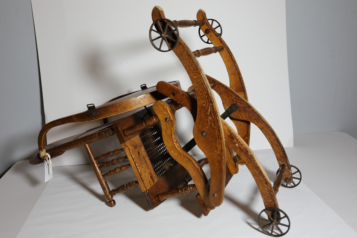 Barnestol med hjul, satt sammen av dreide deler. Stolsete rammer inne et flettet sete. Stolen har et bord festet bak på sidene av stolryggen, det kan vippes bak stolryggen. Stolen står på en ramme som kan endres mellom fire stillinger.  Foran stolen er det en fotstol. Man endrer stilling ved å trekke ut en stang på baksiden og sette endre høyden til et av de fire hakkene. Den nederste stillingen er som gyngestol, stillingen over er som en stasjonær barnestol. De to øverste er som trillende barnestol.