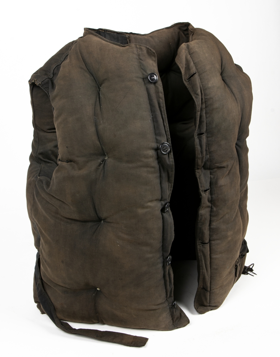 Flytväst Tjockt vadderad mörkbrun flytväst. Enkelknäppt med fem knappar, en ficka på vänster framstycke. Förmodligen vadderad med Kapok.