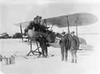 Tre mekaniker framför skidförsedd Phönix D.II. på Flygkompaniet på Malmen, omkring 1922-1926. Motorprovbockar i bakgrunden.