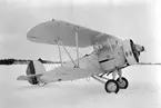 Flygplan B 4 Hawker Hart nr 704 uppställd utanför hangarerna på Centrala verkstäderna Malmen, vintertid 1936. Vy från sidan. Flygplanet var det första av CVM:s licenstillverkade Hawker Hart.