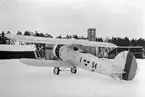 Flygplan B 4 Hawker Hart nr 704 uppställd utanför hangarerna på Centrala verkstäderna Malmen, vintertid 1936. Märkt F 1 nummer 54. Vy snett bakifrån. Flygplanet var det första av CVM:s licenstillverkade Hawker Hart.